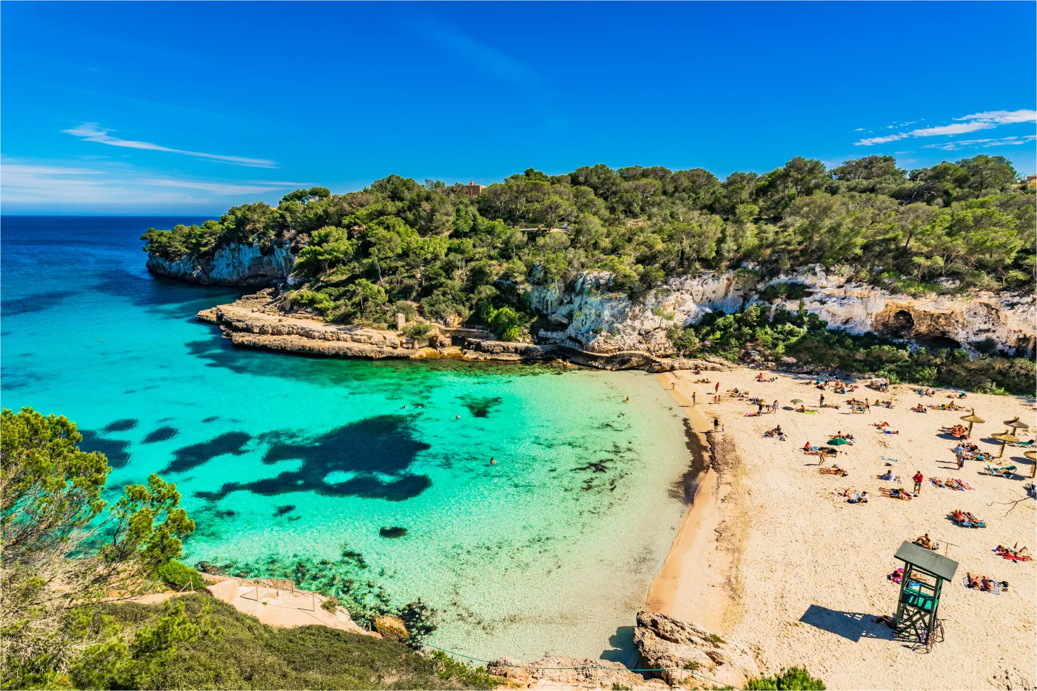 Cala Llombards In Mallorca. People sunbathing on the sand while being surrounded by green rocky cliffs