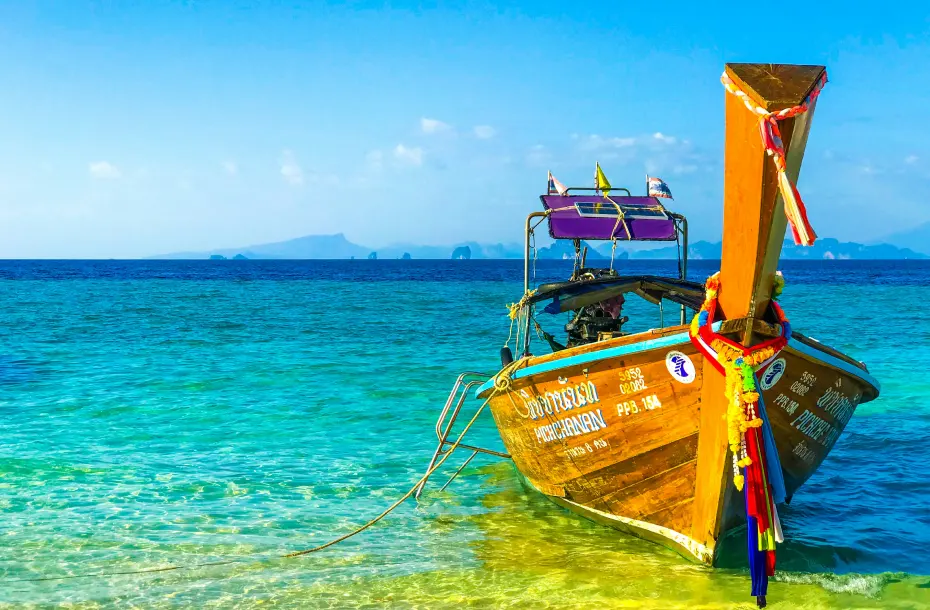 Traditional Thai long-tail boat anchored in the crystal clear turquoise waters of Koh Lanta, Thailand, with distant islands on the horizon.