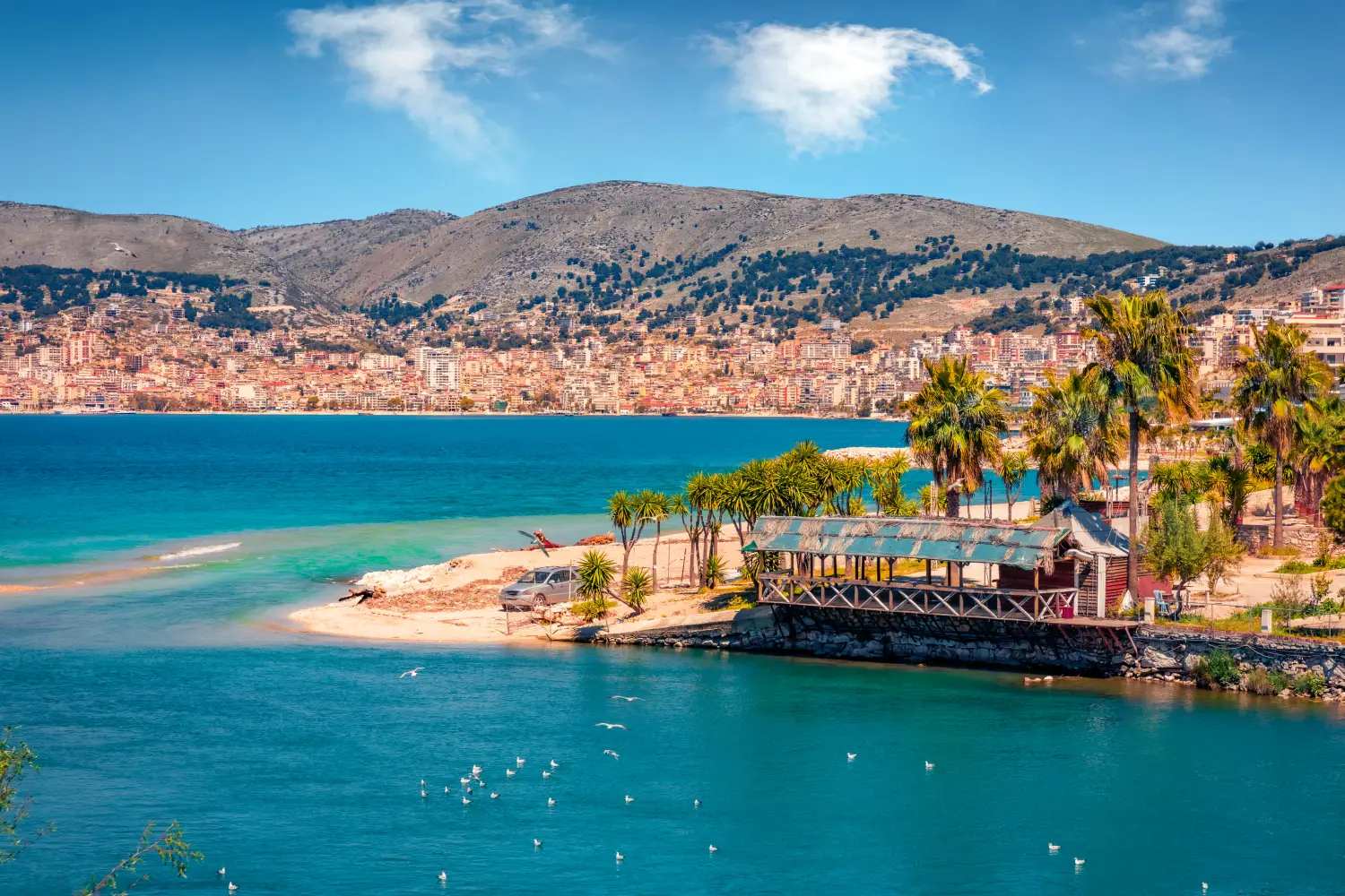 Colorful Spring Cityscape Of Saranda Port. Exotic landscape with palm trees and the city of Saranda in the background