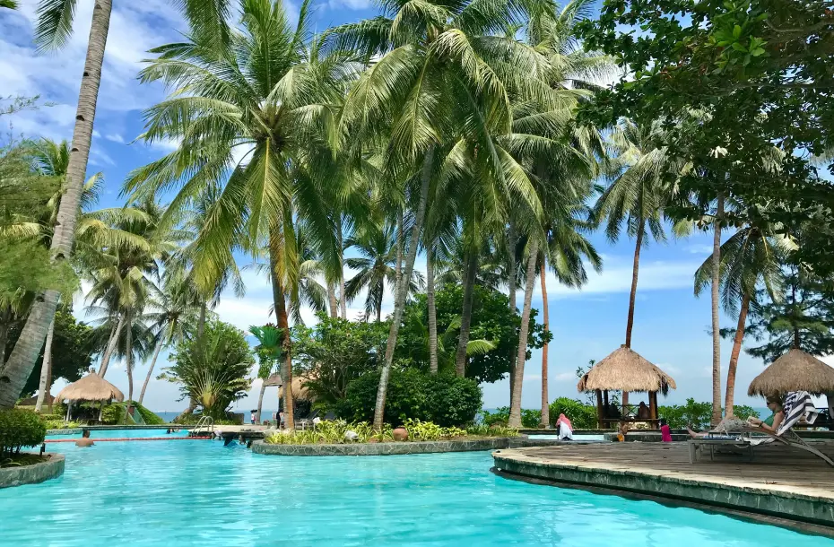 Relaxing vacation scene at a beachfront exotic hotel featuring a turquoise infinity pool, lush greenery and comfortable sun loungers.