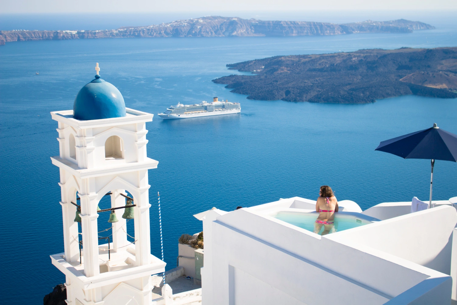 Woman in a terrace pool overlooking the endless blue and the ferry to Santorini, Greece