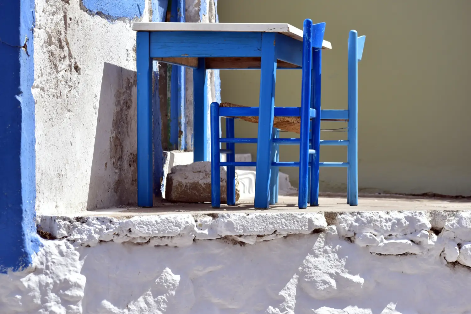 A blue table and a chair outside a traditional house in Pigadia, Karpathos