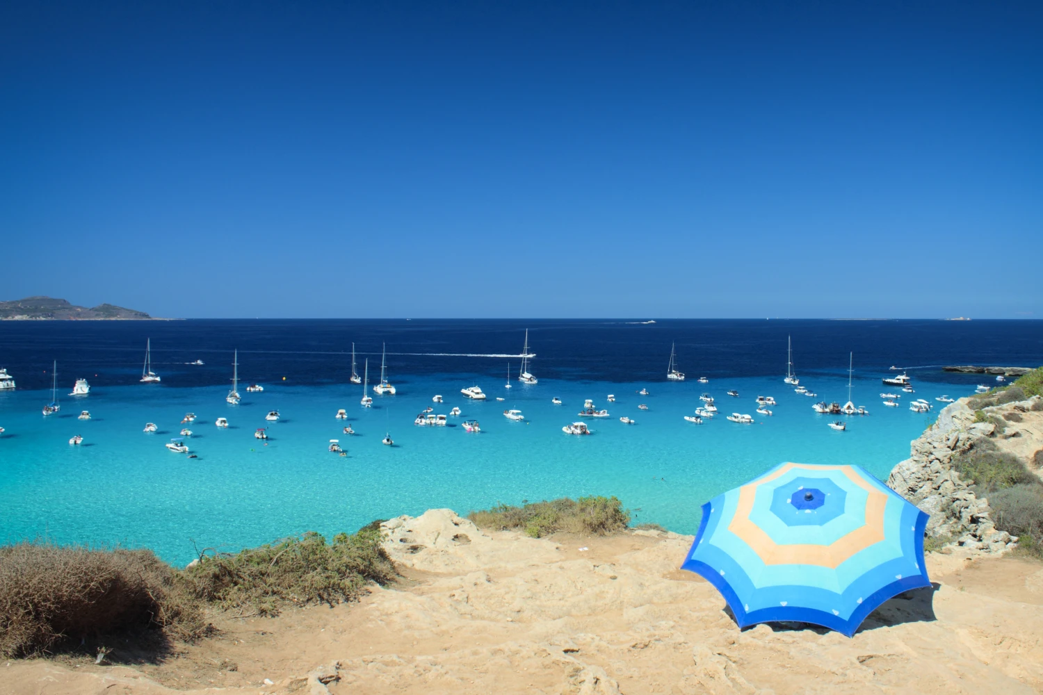 Cala Rossa Beach in Favignana. People under a blue umbrella watching sailing boats